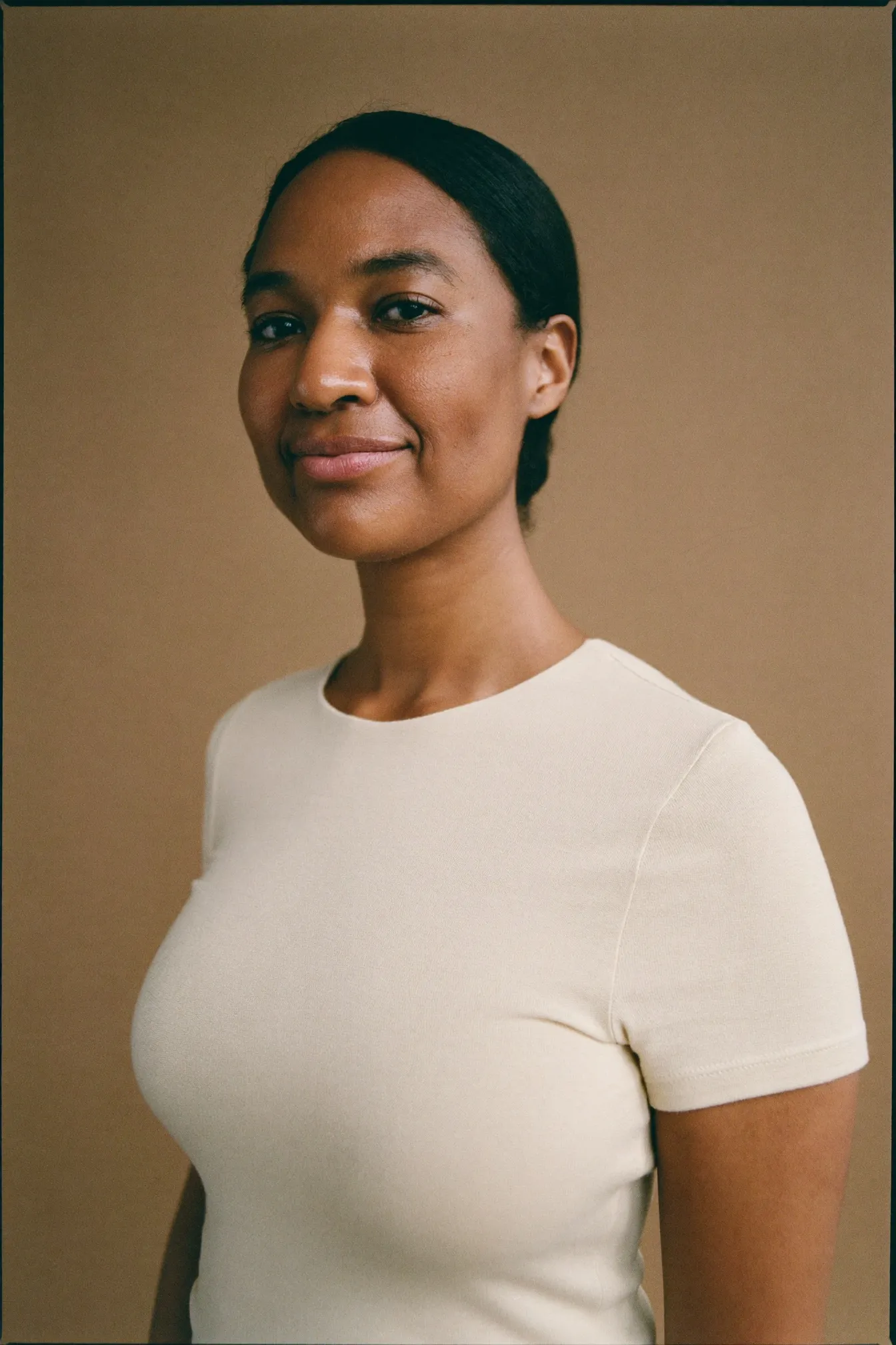 Retrato de estudio de una mujer con camiseta color crudo sobre un fondo de tono arena.