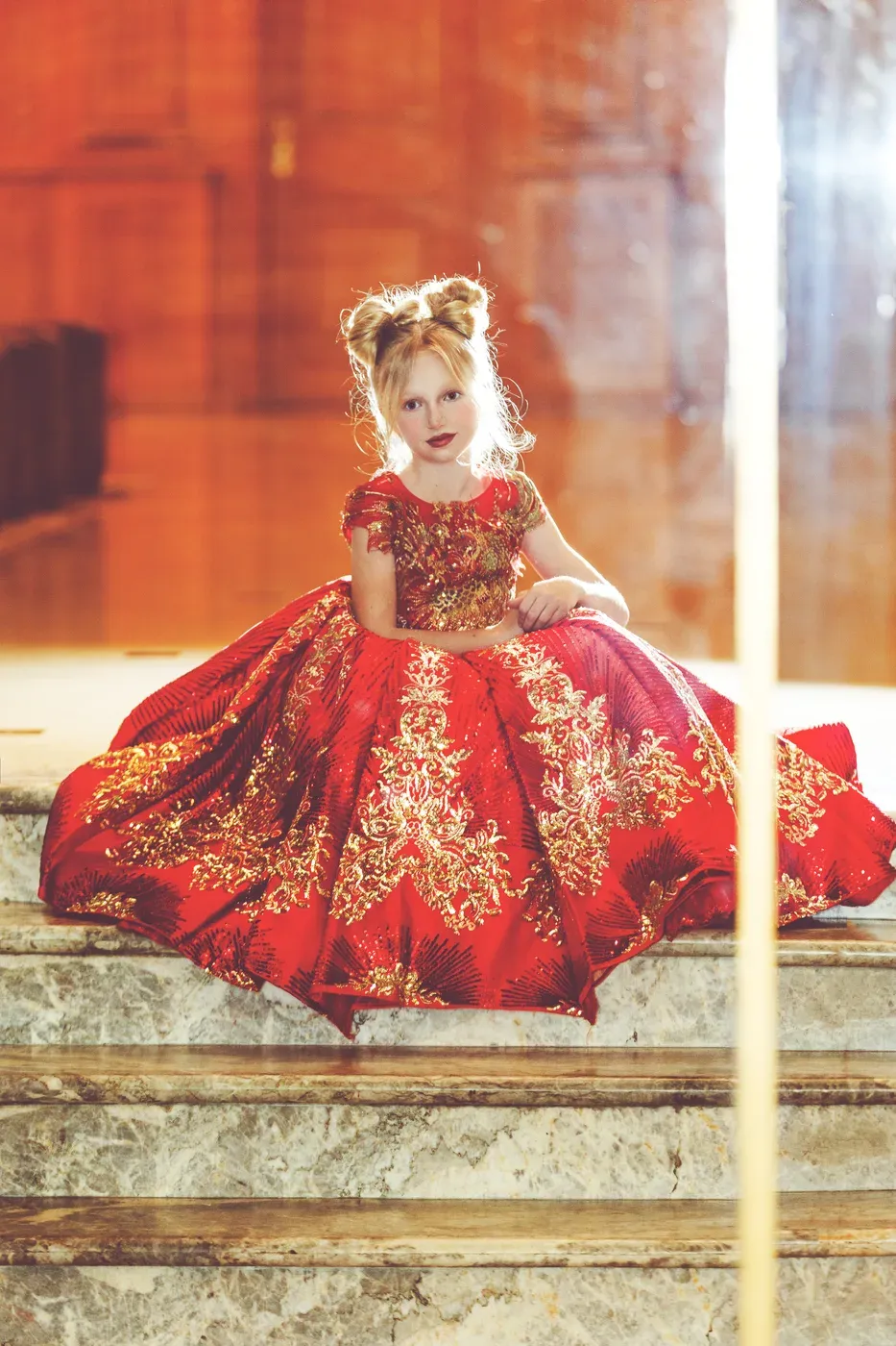 A young model of Be Your Best Academy in a red and gold couture gown during an editorial photoshoot in Marbella.